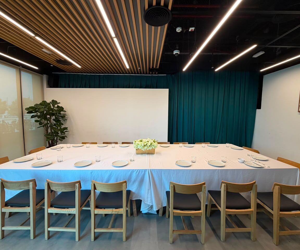 The Room set up with a long dining table, white tablecloth and wooden chairs in front of a teal curtain